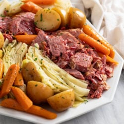 Tender Corned Beef and Cabbage on a white platter with carrots and potatoes.