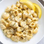 Garlic Butter Pasta on a white plate with an herb sauce on top and slices of lemon on the side.