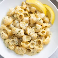 Garlic Butter Pasta on a white plate with an herb sauce on top and slices of lemon on the side.
