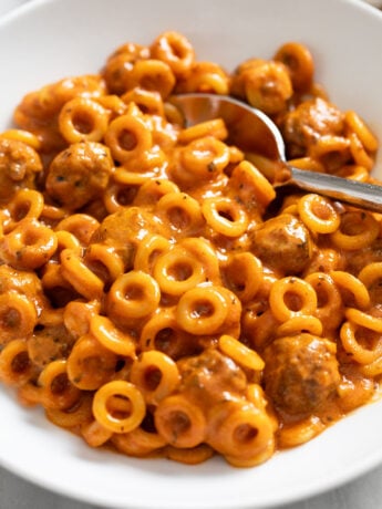 A white bowl filled with Homemade Spaghettios with a spoon in the back.