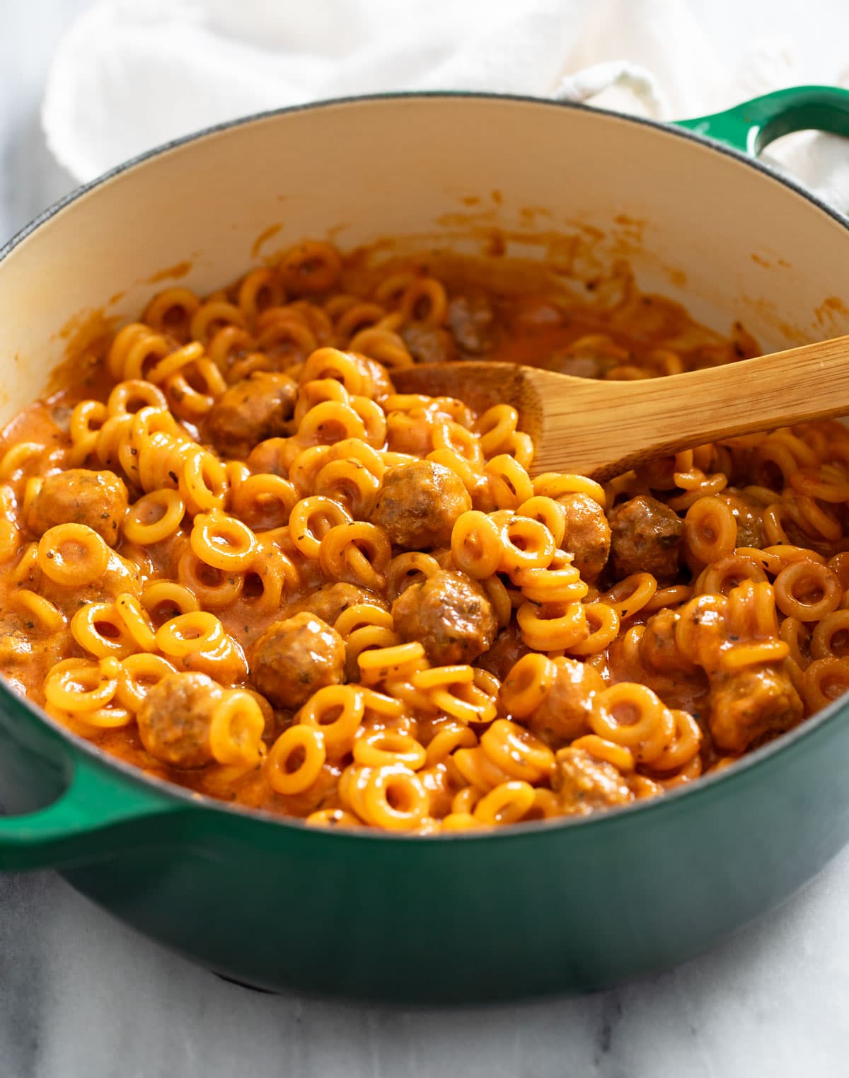 A green Dutch oven filled with Homemade Spaghettios with a wooden spoon.