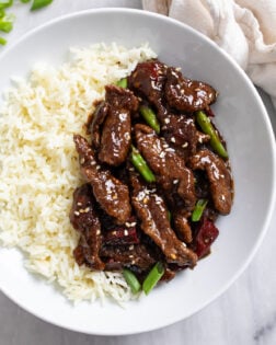 Mongolian Beef in a white bowl with rice and sliced green onions.