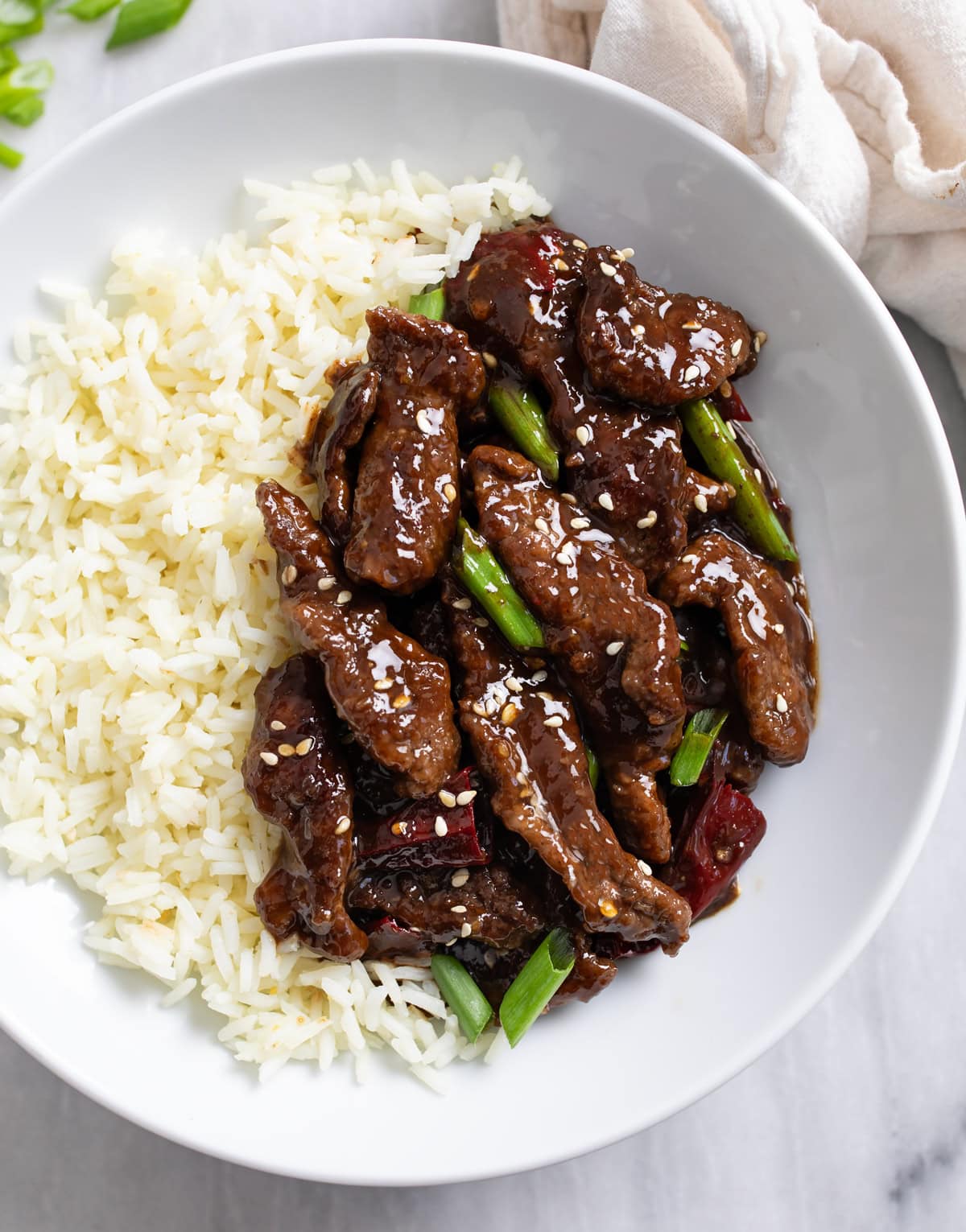 Mongolian Beef in a white bowl with rice and sliced green onions.