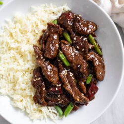 A bowl of Mongolian Beef and white rice with sliced green onions and toasted sesame seeds.