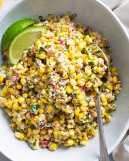 Mexican Street Corn Salad in a white bowl with lime wedges and a spoon on the side.