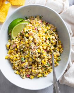 Mexican Street Corn Salad in a bowl with Cotija cheese on top and a spoon on the side.
