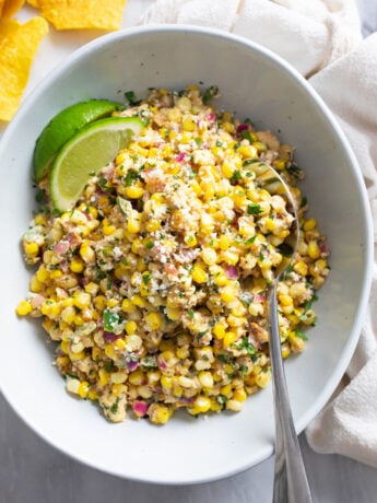 Mexican Street Corn Salad in a bowl with Cotija cheese on top and a spoon on the side.
