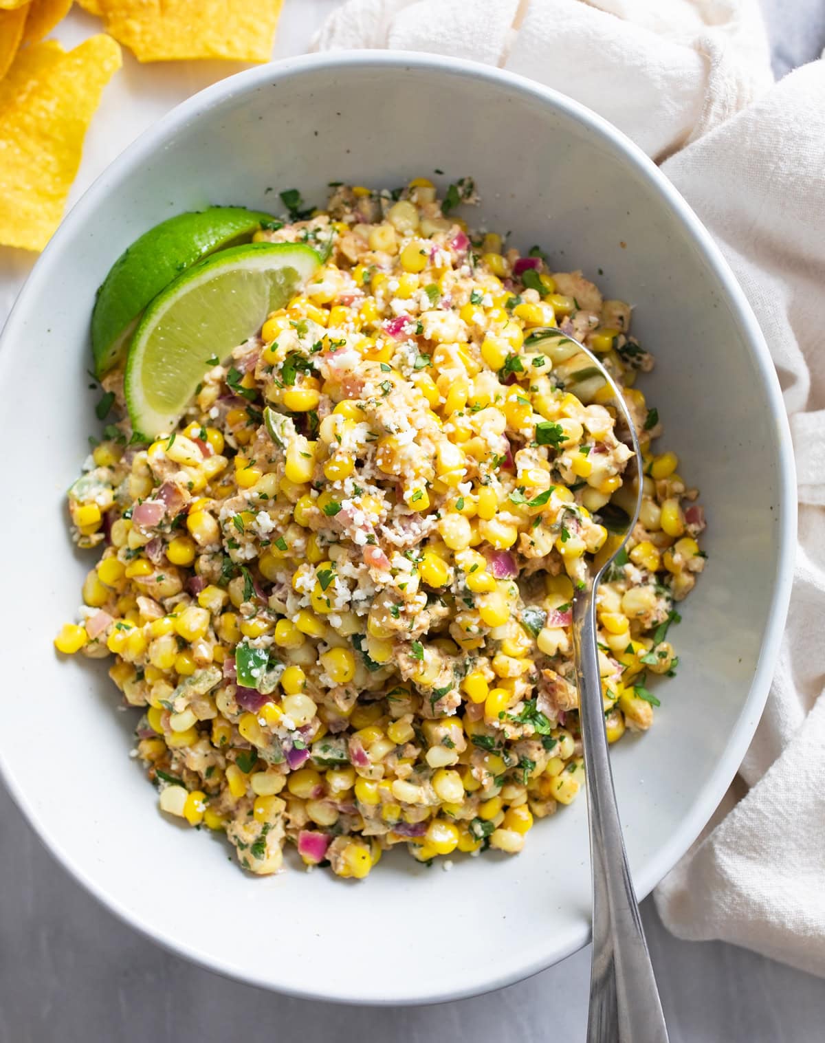 Mexican Street Corn Salad in a bowl with Cotija cheese on top and a spoon on the side.