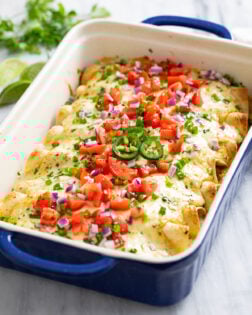 White Chicken Enchiladas in a baking dished topped with diced tomatoes, green and red onions, cilantro, and jalapenos.