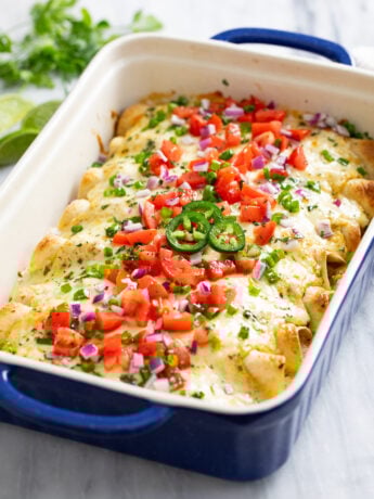 White Chicken Enchiladas in a baking dished topped with diced tomatoes, green and red onions, cilantro, and jalapenos.
