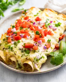 Cheesy White Chicken Enchiladas on a plate with lime wedges and cilantro on the side.