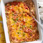 Bean Dip in a baking dish with a serving spoon on the side and toppings on top.
