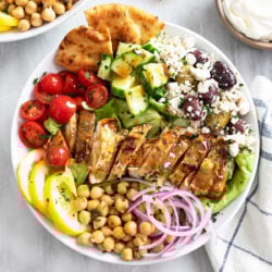 Overhead view of Greek Chicken Bowls in a white bowl with vegetables, olives, feta, and chickpeas.