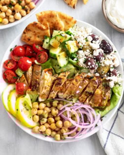 Overhead view of Greek Chicken Bowls in a white bowl with vegetables, olives, feta, and chickpeas.