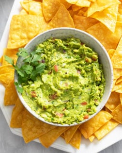 Homemade Guacamole in a bowl with fresh cilantro on the side and tortilla chips around it.