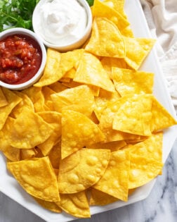 Homemade Tortilla Chips on a white platter with ramekins of sour cream and salsa.
