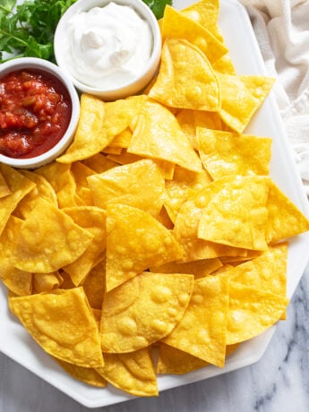 Homemade Tortilla Chips on a white platter with ramekins of sour cream and salsa.