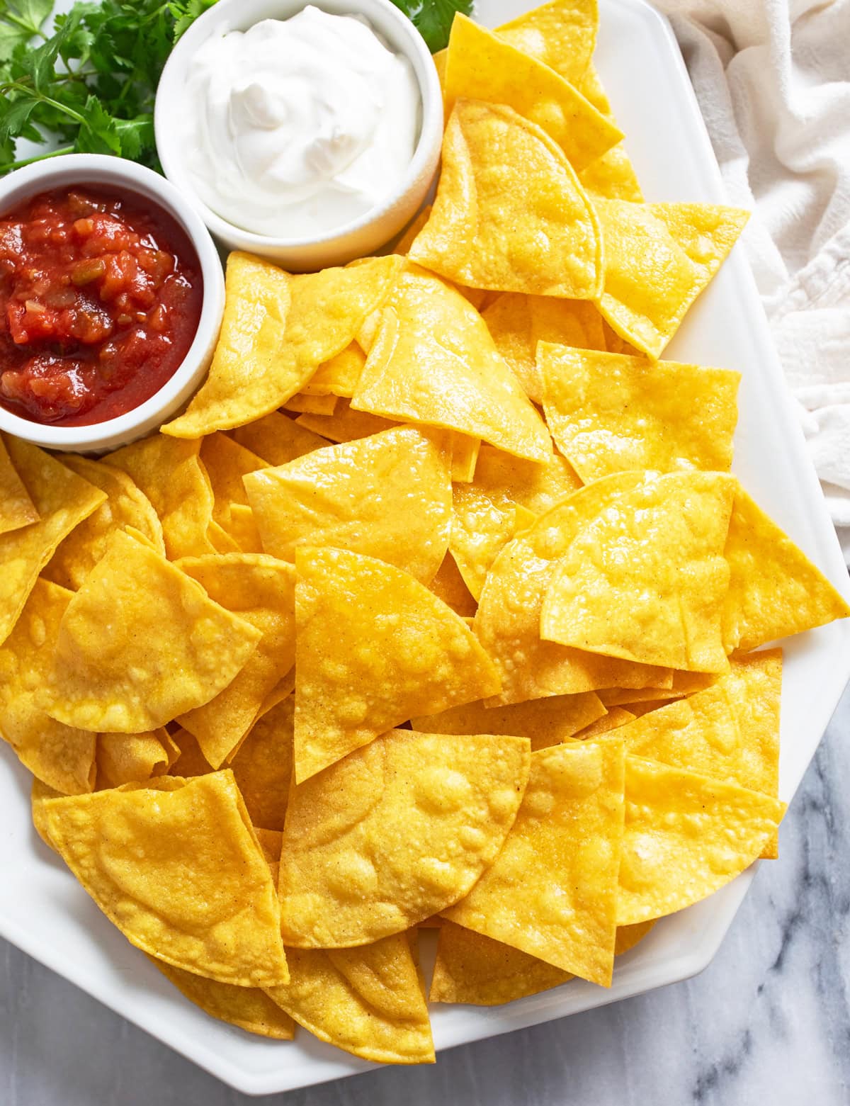 Homemade Tortilla Chips on a white platter with ramekins of sour cream and salsa.