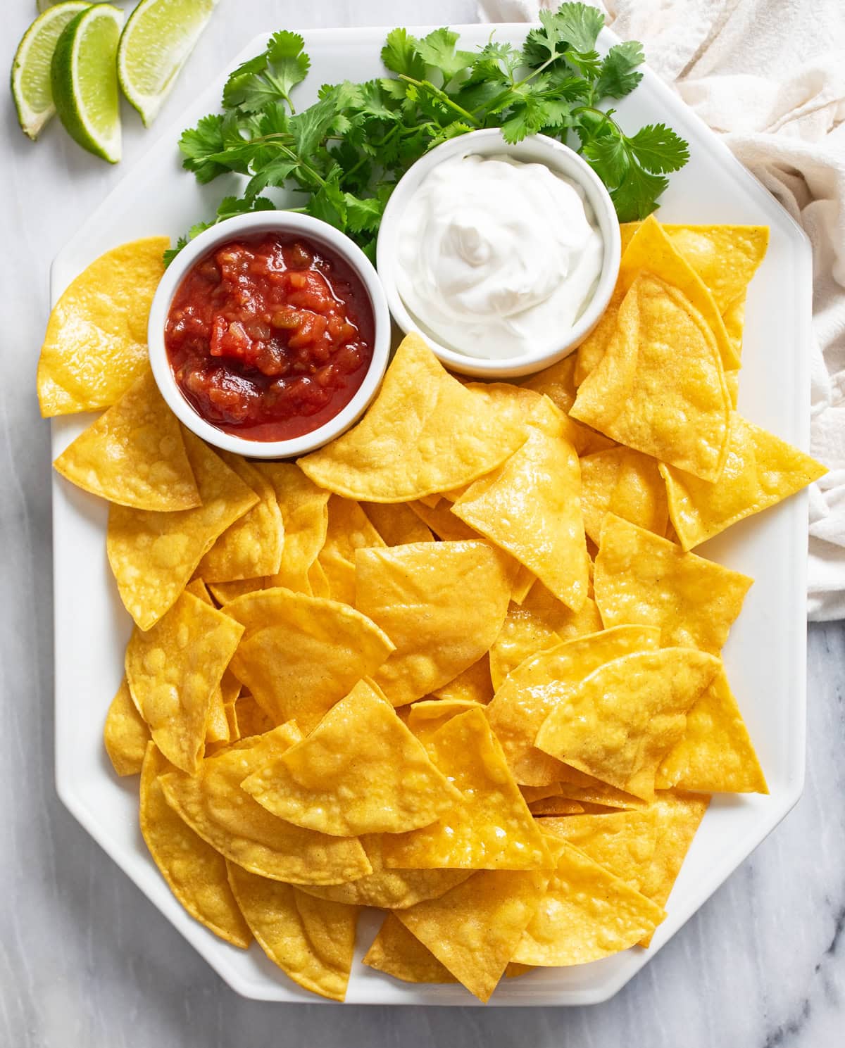 Homemade Tortilla Chips on a white platter with cilantro, salsa, and sour cream.