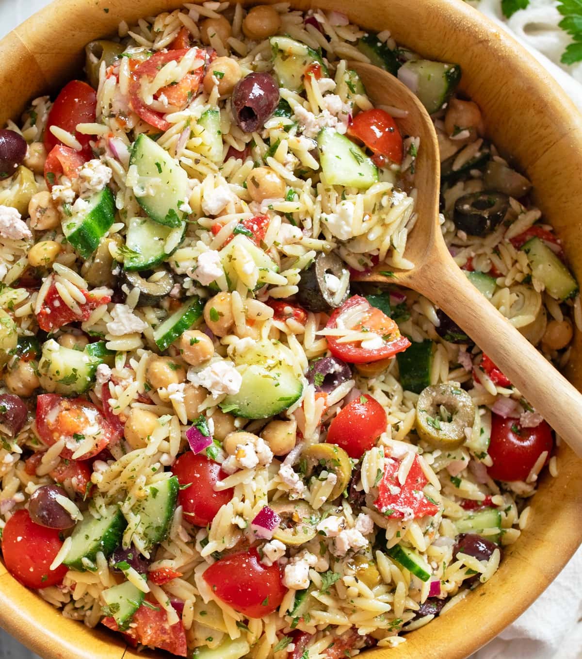 Orzo Salad in a wooden bowl with a wooden spoon and Mediterranean ingredients.