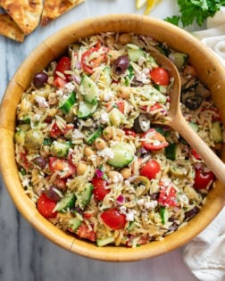 Orzo Salad in a wooden bowl with Mediterranean ingredients and a wooden spoon on the side.
