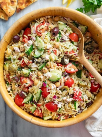 Orzo Salad in a wooden bowl with Mediterranean ingredients and a wooden spoon on the side.