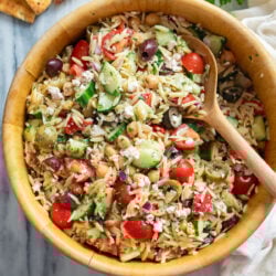 Orzo Salad in a wooden bowl with tomatoes, cucumbers, olives, feta, chickpeas, and more.