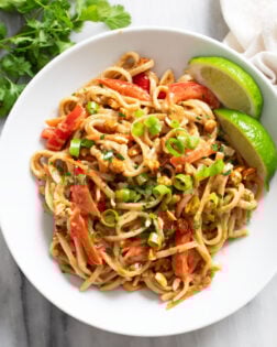 Peanut Butter Noodles in a white bowl with slices of lime on the side and green onions on top.