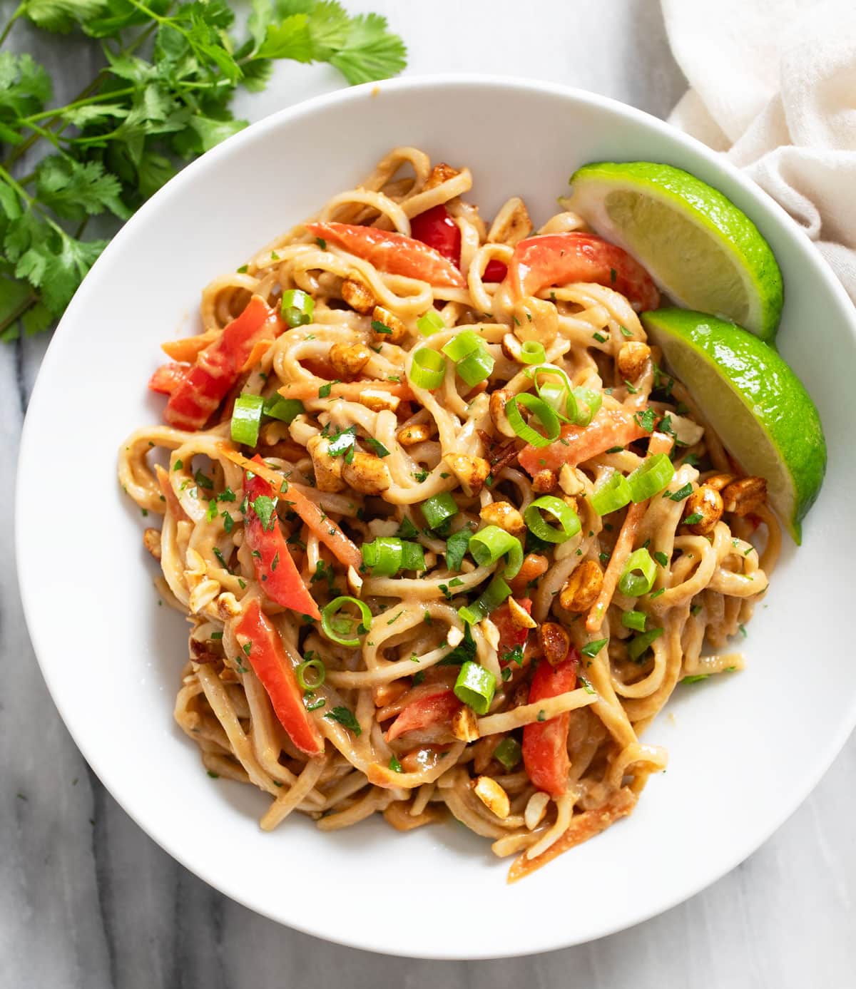 Peanut Butter Noodles in a white bowl with slices of lime on the side and green onions on top.