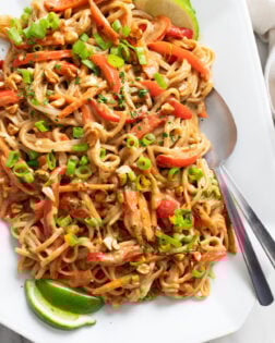 Peanut Butter Noodles on a white tray with green onions on top and lime slices on the side.