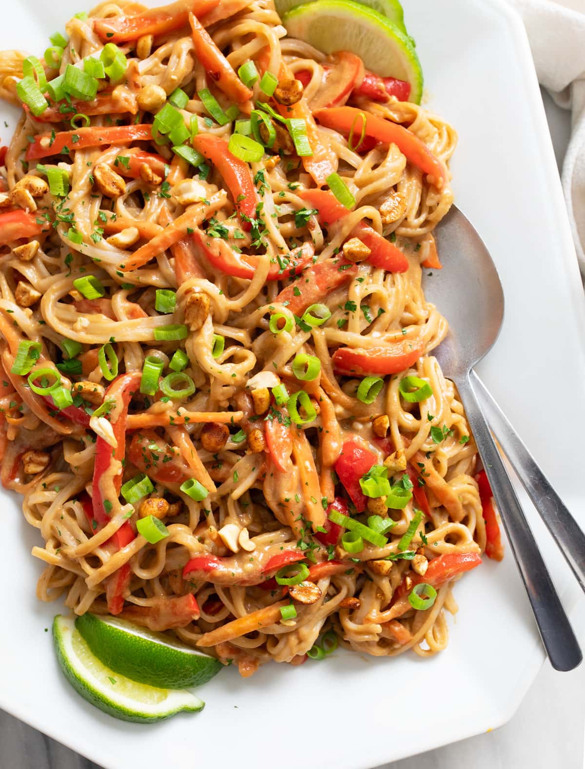 Peanut Butter Noodles on a white tray with green onions on top and lime slices on the side.