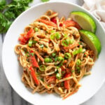 Peanut Butter Noodles in a white bowl with vegetables and lime wedges on the side.