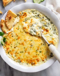 Spinach and Artichoke Dip in a white serving dish with a spoon and pita bread on the side.