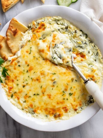 Spinach and Artichoke Dip in a white serving dish with a spoon and pita bread on the side.