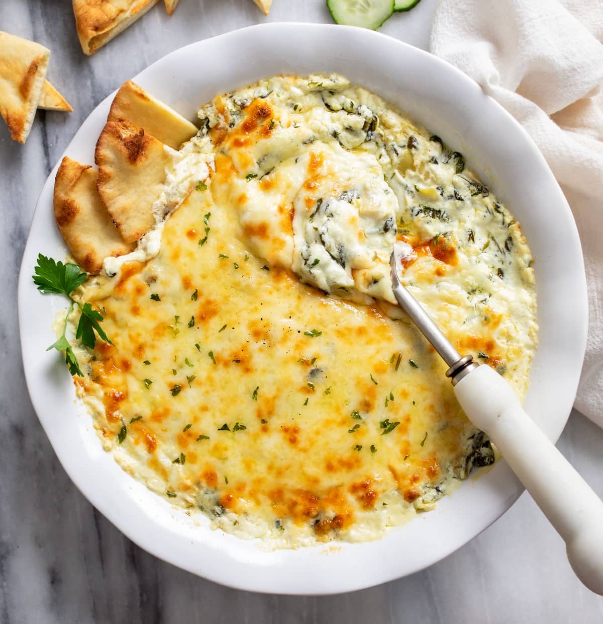 Spinach and Artichoke Dip in a white serving dish with a spoon and pita bread on the side.