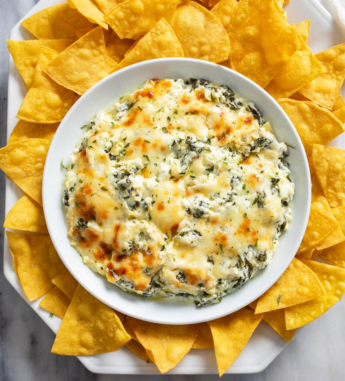 Spinach and Artichoke Dip in a white bowl with tortilla chips around it.