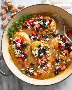 Balsamic Chicken in a skillet with feta and blueberries and strawberries on top an a spoon on the side.