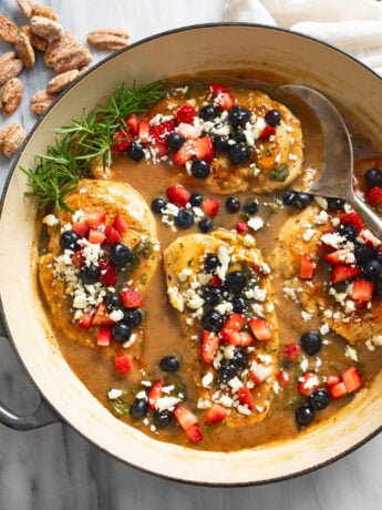 Balsamic Chicken in a skillet with feta and blueberries and strawberries on top an a spoon on the side.