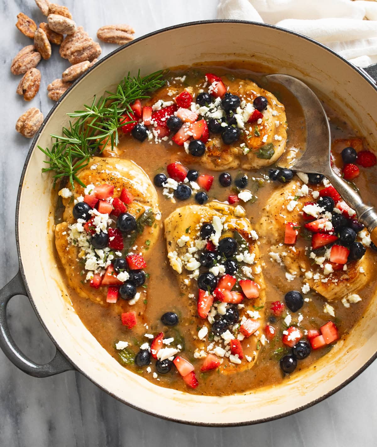 Balsamic Chicken in a skillet with feta and blueberries and strawberries on top an a spoon on the side.
