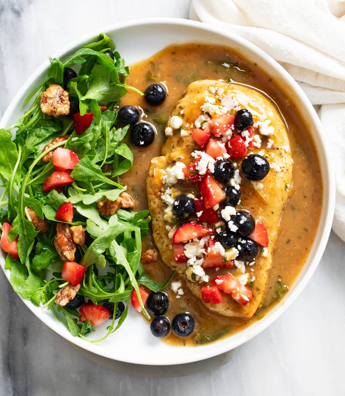 Balsamic Chicken on a white plate with sauce, berries, feta, arugula, and pecans.