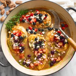 A skillet of Balsamic Chicken with berries and feta on top with fresh rosemary on the side.