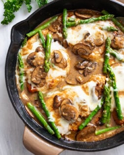 Chicken Madeira in a skillet with a Madeira mushroom sauce with melted mozzarella and asparagus.