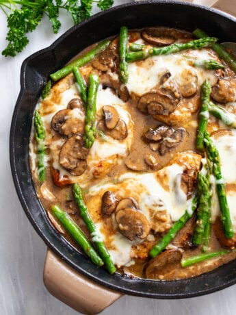 Chicken Madeira in a skillet with a Madeira mushroom sauce with melted mozzarella and asparagus.