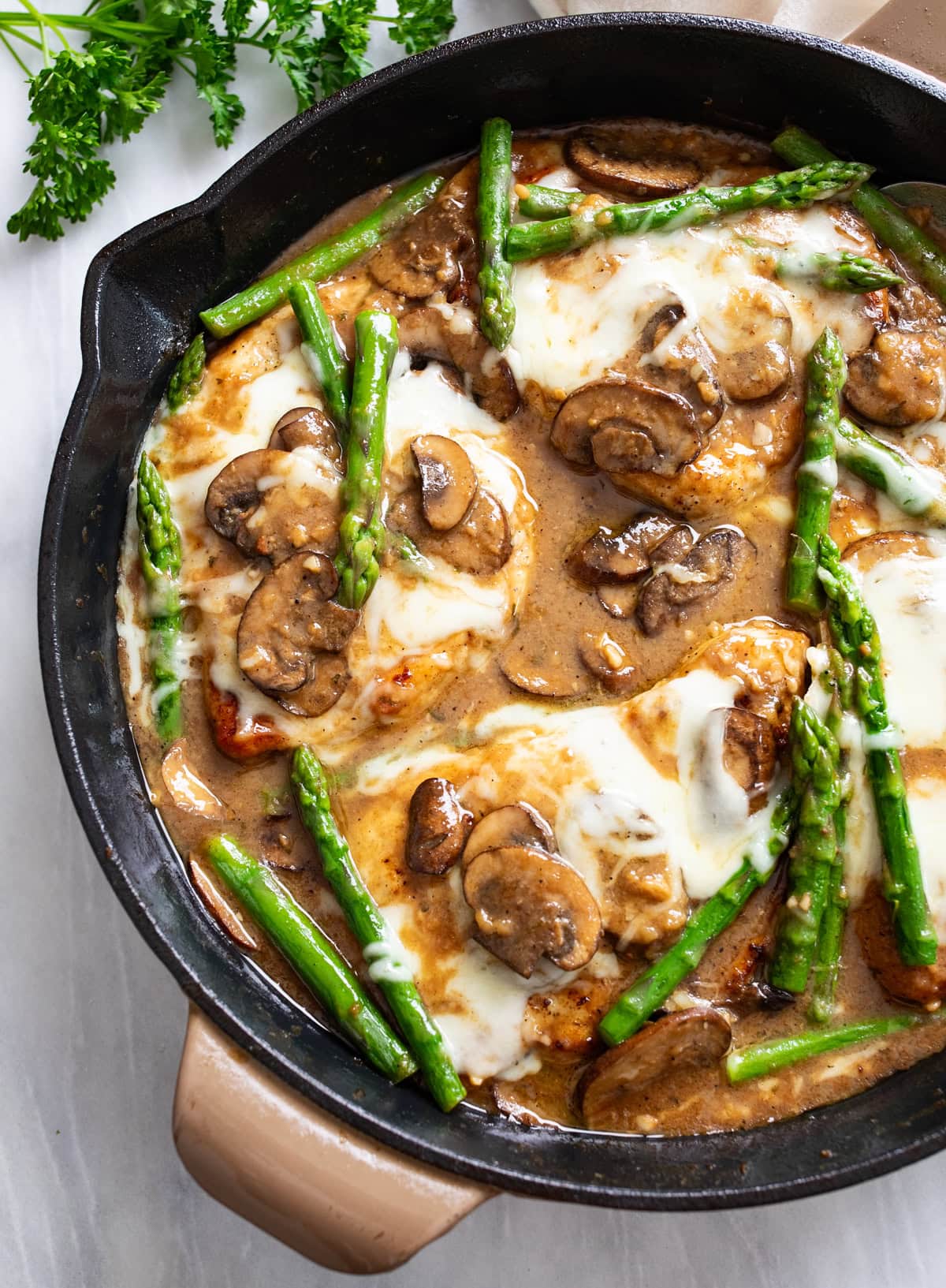Chicken Madeira in a skillet with a Madeira mushroom sauce with melted mozzarella and asparagus.
