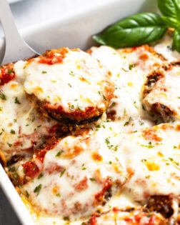 Eggplant Casserole in a baking dish with marinara sauce and melted mozzarella with fresh basil on the side.