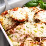 Eggplant Casserole in a baking dish with marinara sauce and melted mozzarella with fresh basil on the side.