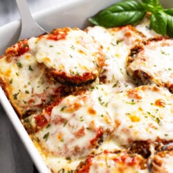 Eggplant Casserole in a baking dish with marinara sauce and melted mozzarella with fresh basil on the side.