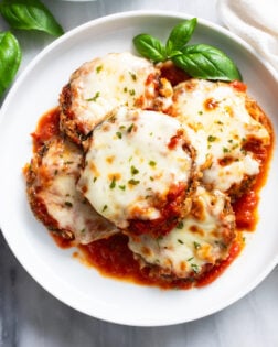 Eggplant Parmesan on a white plate with marinara sauce and fresh basil.