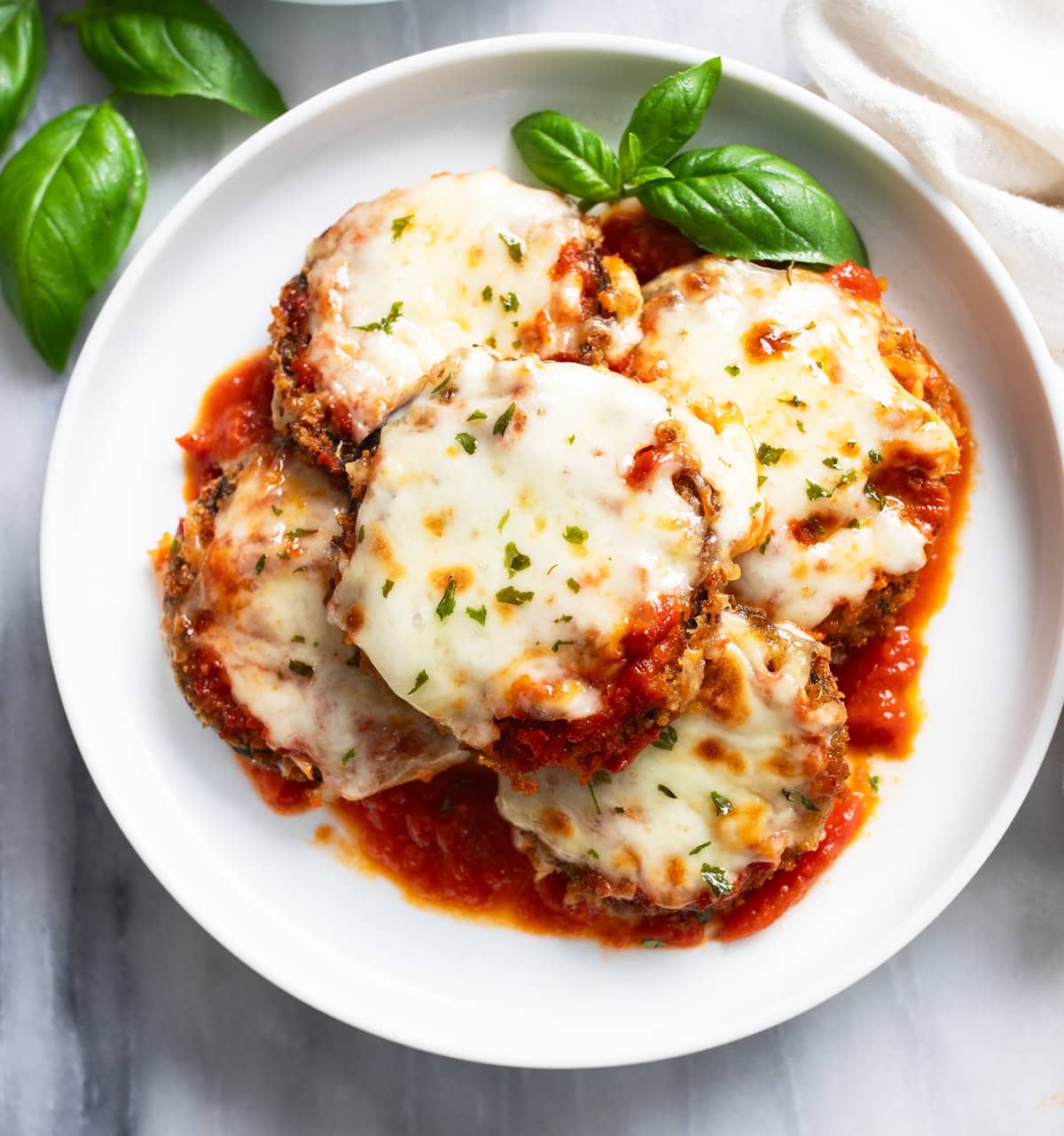 Eggplant Parmesan on a white plate with marinara sauce and fresh basil.