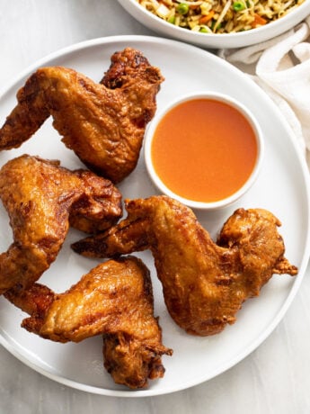 Fried Chinese Chicken Wings on a white plate with sweet and sour sauce on the side.